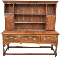 AN 18TH CENTURY OAK DRESSERThe cornice above a shaped apron and shelves and two cupboard doors above