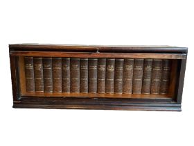A COLLECTION OF SIXTEEN LEATHER BOUND CHARLES DICKENS BOOKS, DISPLAYED IN GLOBES STYLE BOOKCASE.