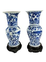 A PAIR OF CHINESE BLUE AND WHITE VASES ON PIERCED WOODEN BASES, BOTH BEARING SIX CHARACTER KANGXI