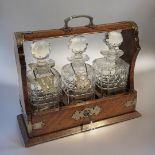 AN EARLY 20TH CENTURY OAK AND CUT GLASS TANTALUS Having silver plated corners, Bramah lock and three