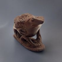 A JAPANESE WOODEN TOAD NETSUKE Sat on a sandal with maker’s mark to base. (5.5cm x 3cm x 4cm)