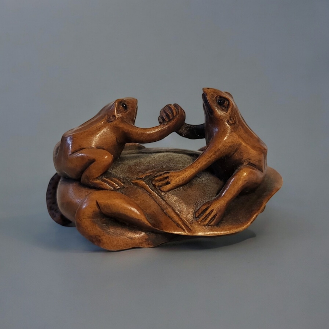 A 20TH CENTURY JAPANESE CARVED WOODEN NETSUKE Two frogs shaking hands on a lily pad, signed to base.