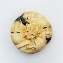 A JAPANESE BONE NETSUKE Circular form, with carved stylised faces to body. (4cm x 1.5cm)