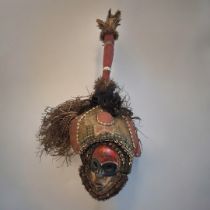 AN AFRICAN TRIBAL CARVED WOODEN DAN MASK/HEADDRESS Having feathers to finial, carved wooden red