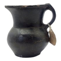 A SOUTH AMERICAN BLACKWARE POTTERY JUG Having a single handle and inlaid metallic mounts to rim. (