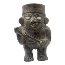 A SOUTH AMERICAN POTTERY FIGURAL JUG Having painted eyes and clutching a war club and metal nose