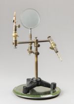 A VINTAGE BRASS MAGNIFYING GLASS ON TRIPOD BASE. Adjustable, with alligator clips, displayed on