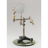 A VINTAGE BRASS MAGNIFYING GLASS ON TRIPOD BASE. Adjustable, with alligator clips, displayed on