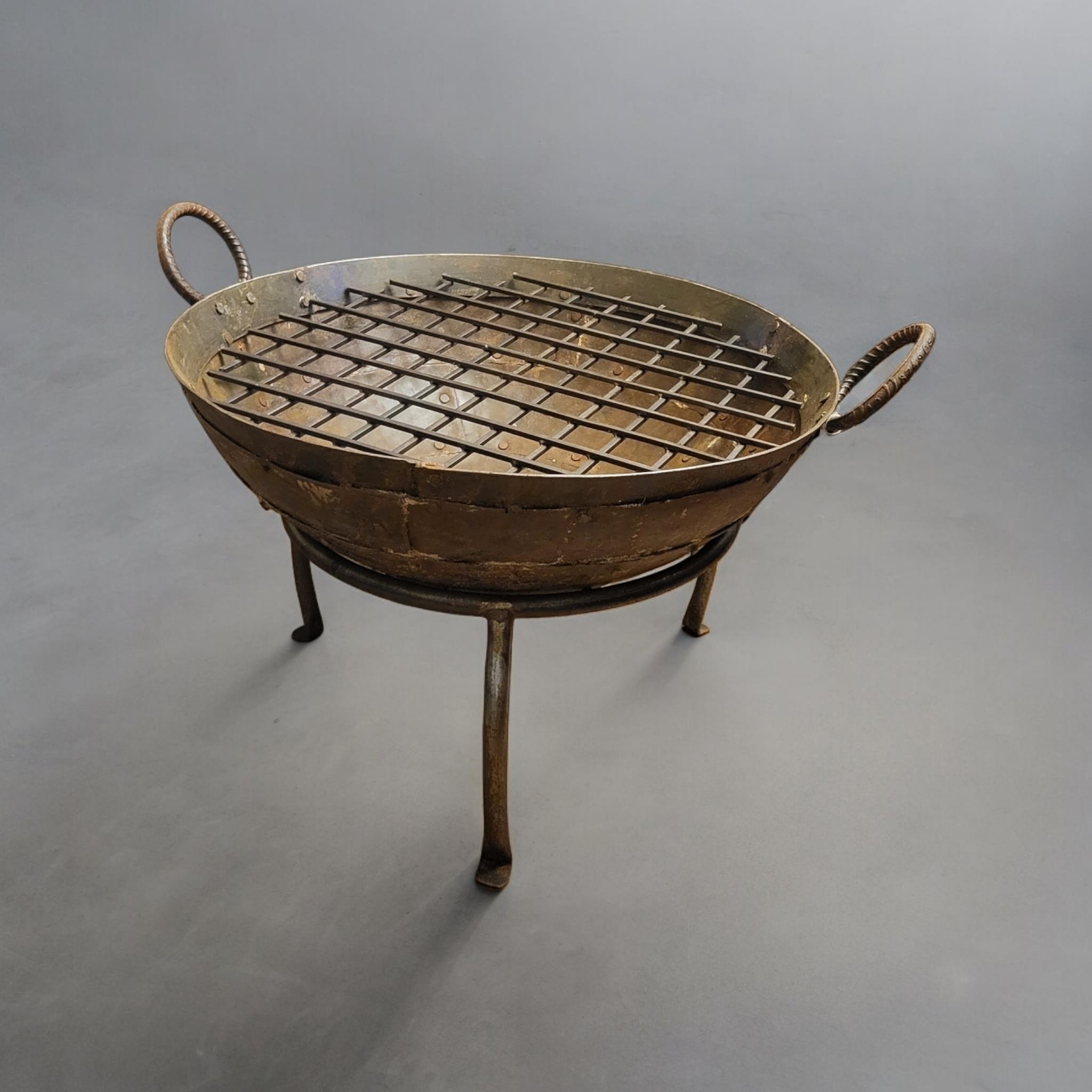 A CAST IRON FIRE PIT With ring handles and riveted body, inserted griddle and detachable tripod