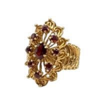 A VINTAGE YELLOW METAL AND GARNET CLUSTER RING Having an oval cut central stone edged with round cut