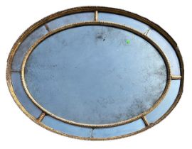 MANNER OF ROBERT ADAM, A GEORGE III OVAL CARVED GILTWOOD SECTIONAL MIRROR With original mercury
