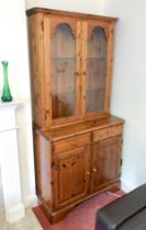 A Ducal pine glazed cupboard bookcase or dresser - the moulded top over a pair of arched glazed