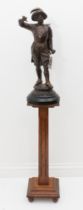 A patinated spelter figure of a cavalier on an oak pedestal stand. The figure with brown patinated