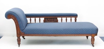 A late Victorian oak chaise longue - the foliate and scroll carved arm and turned spindle back