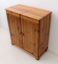 A pine two-door cupboard - the moulded top over panelled doors enclosing a single shelf, on turned