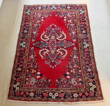 A Persian rug - with a large floral medallion and spandrels on a madder ground, within a blue floral