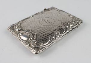 A large silver card case with planished finish and bold scrolling border, engraved initials M.H.