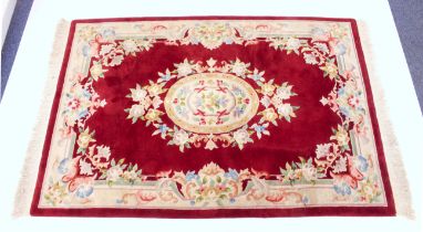 A Chinese wool rug - with a single oval floral and ribbon medallion and floral spandrels, on a