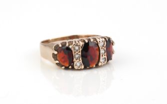 A 9ct rose gold, garnet and white stone ring - the three graduated oval cut garnets divided by trios