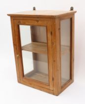 An antique glazed pine wall hanging display cabinet - with glazed door and sides, later brass