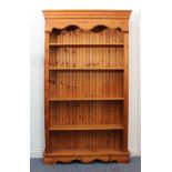 A modern pine open bookcase - the ogee moulded cornice over a serpentine frieze, above four