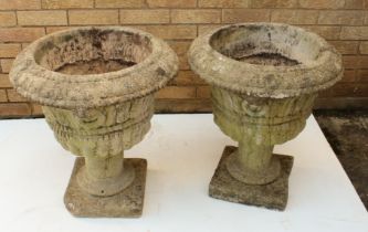 A pair of composite stone garden urns - with stiff leaf and gadrooned decoration and mask handles,