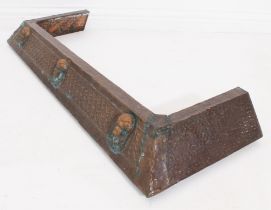 An Edwardian hammered copper fire curb - of bevelled form, decorated with three classical masks