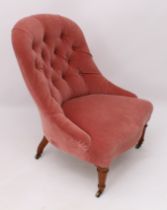 An Edwardian tub back low armchair - the buttoned back and seat in pink velour, raised on turned and