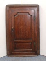 A mid-18th century oak wall-hanging corner cupboard - with two-panel door and fluted canted corners,