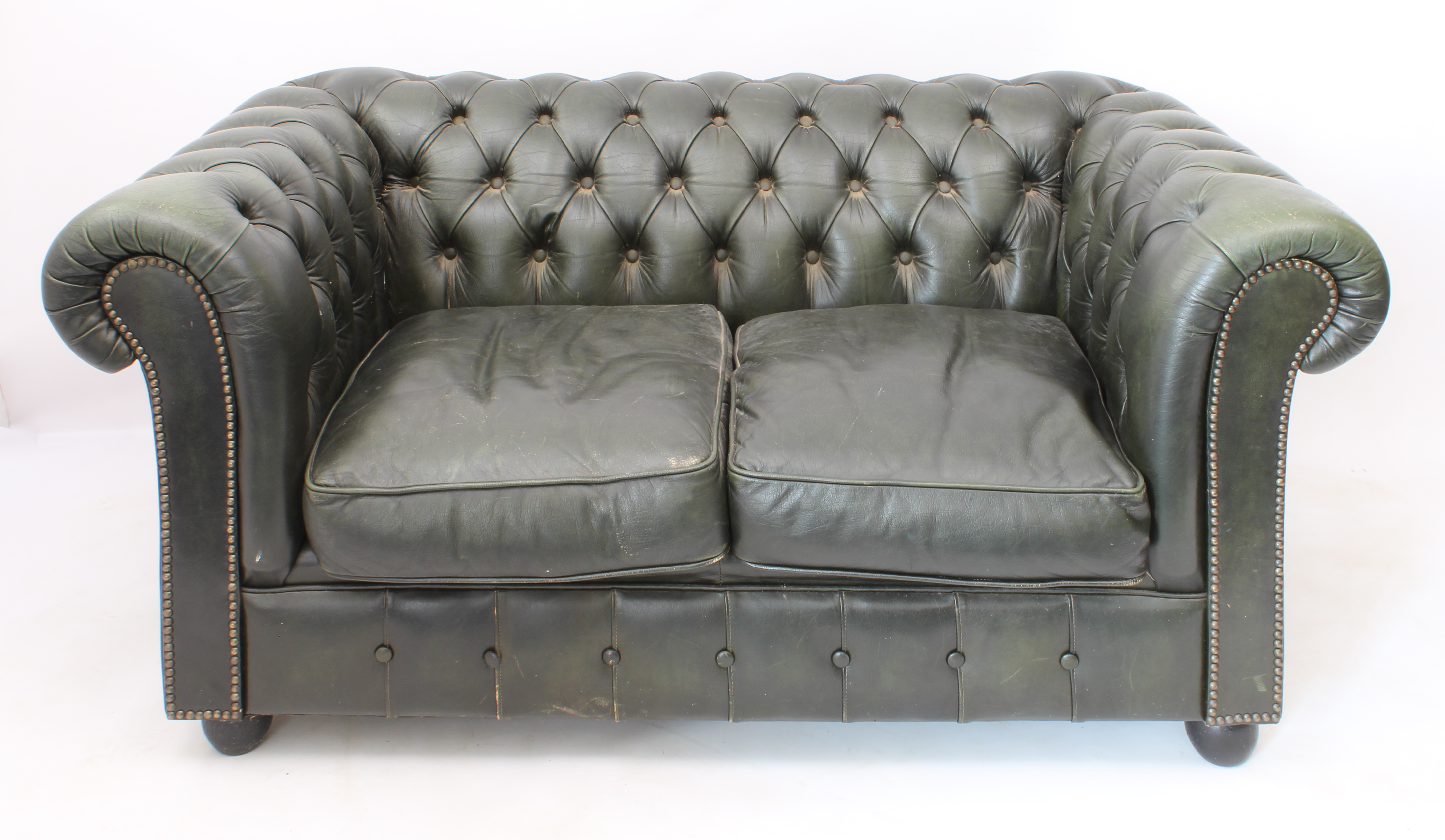 A green leather two-seater Chesterfield sofa - raised on four bun feet (LWH 148 x 87 x 71 cm)