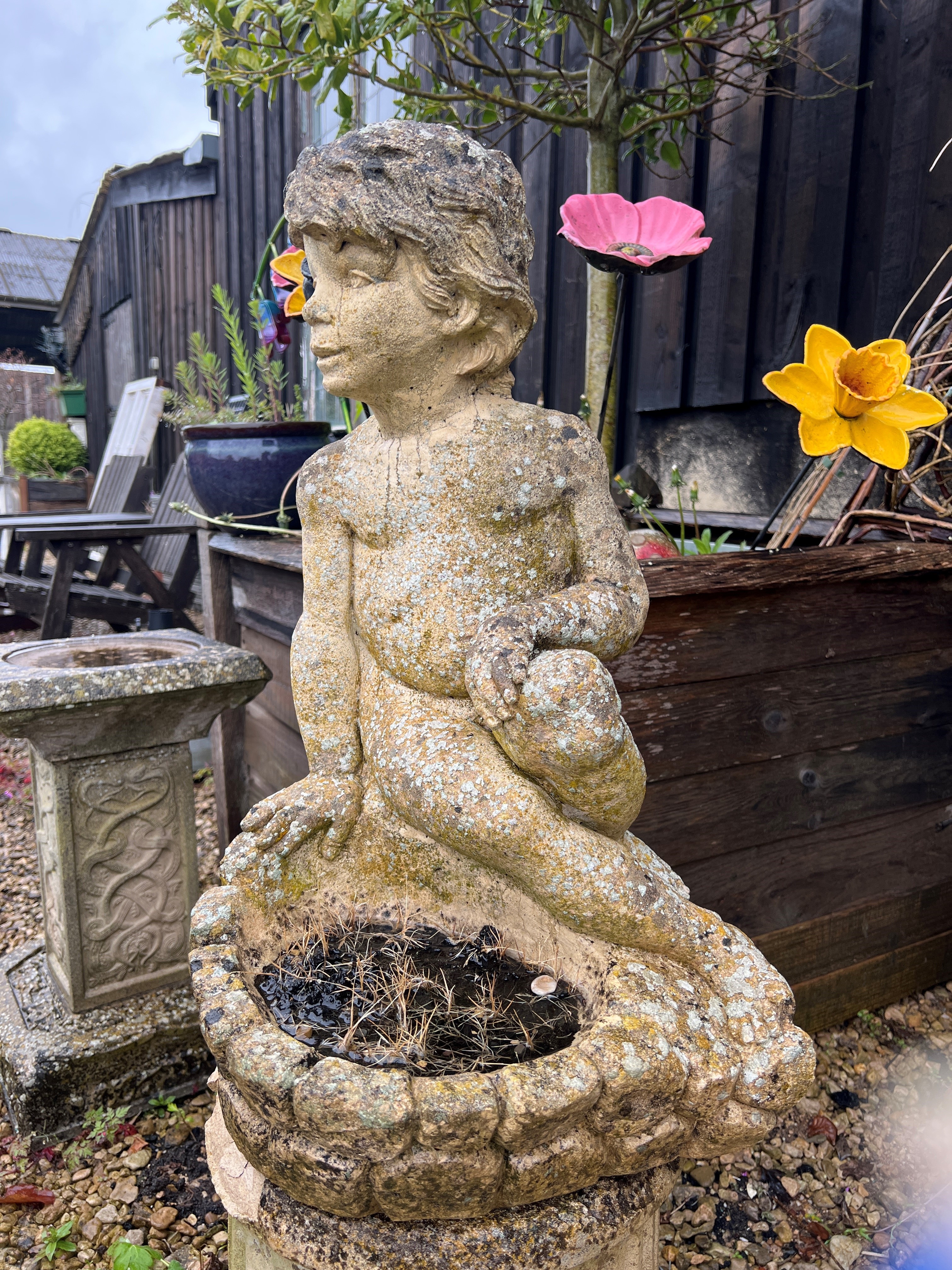 A composite stone garden statue of a seated boy - 64cm high.