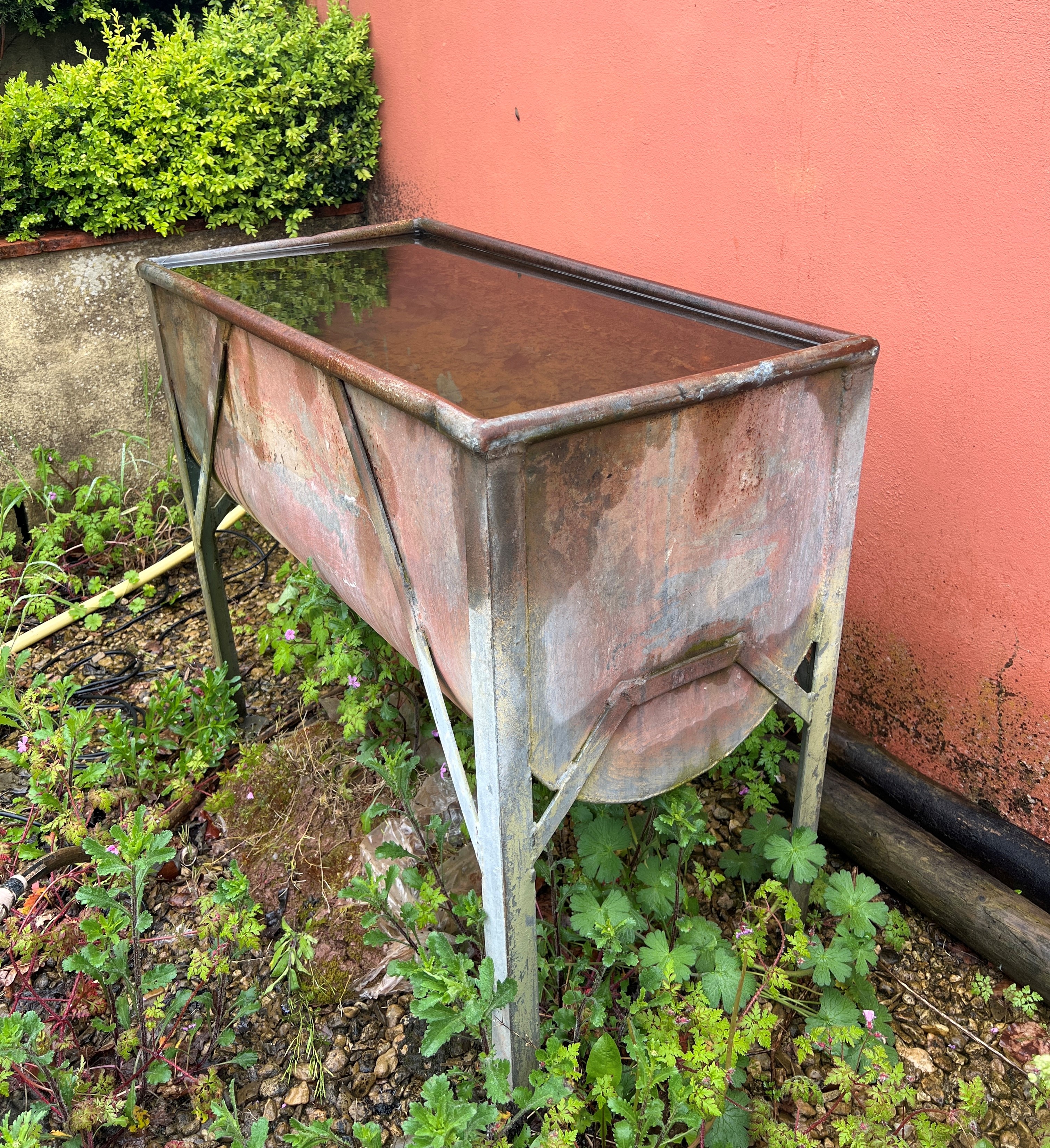 A galvanised metal water trough - with cylinder base, on four legs, 93 x 49cm, 83cm high.