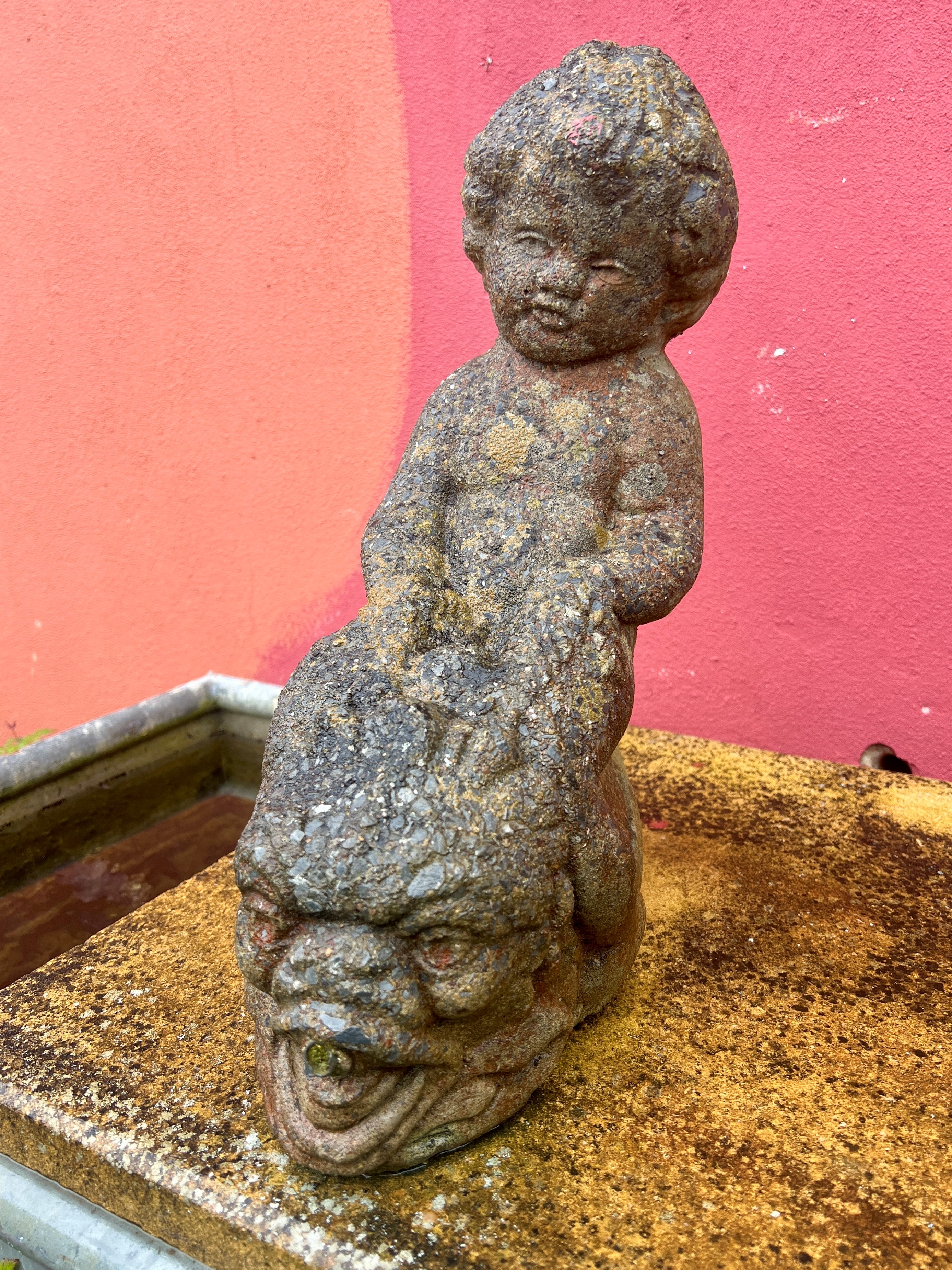 A composite stone garden statue of a child astride a dolphin - 29 x 15cm, 39cm high.