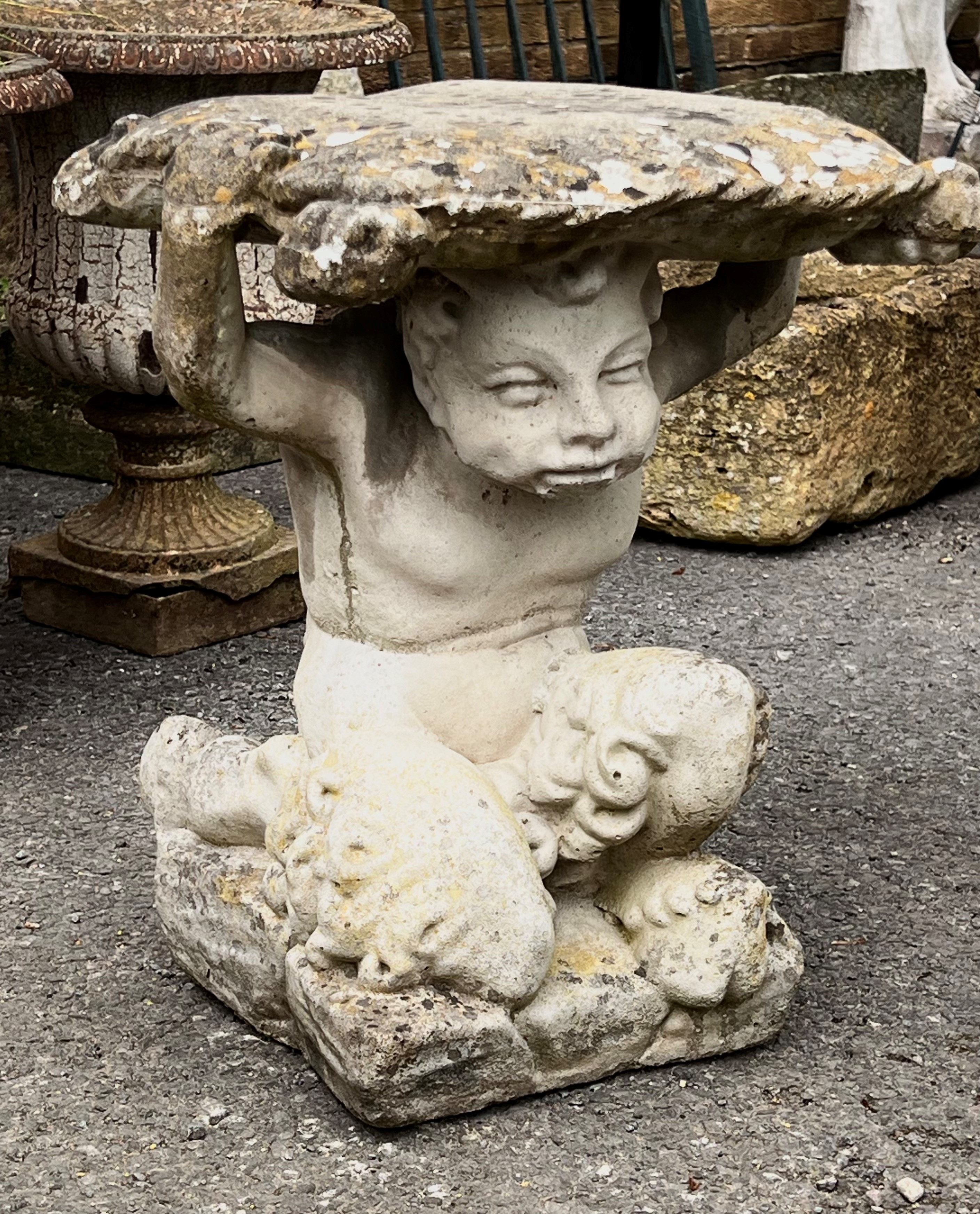 A small composite stone garden table or plinth - in the form of a figure of a boy supporting a