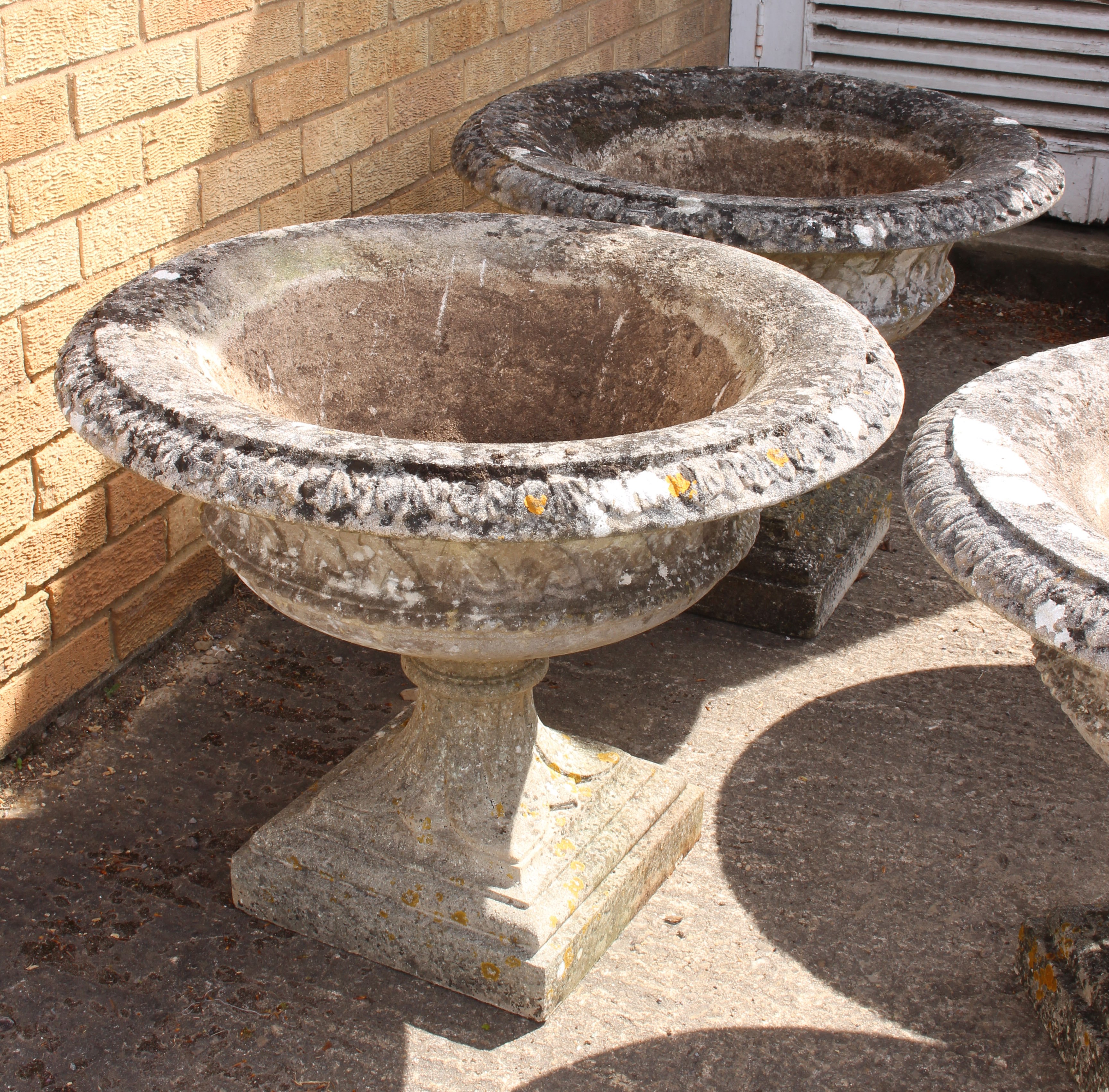 A pair of large composite stone campana style garden urns - well weathered, decorated with foliage