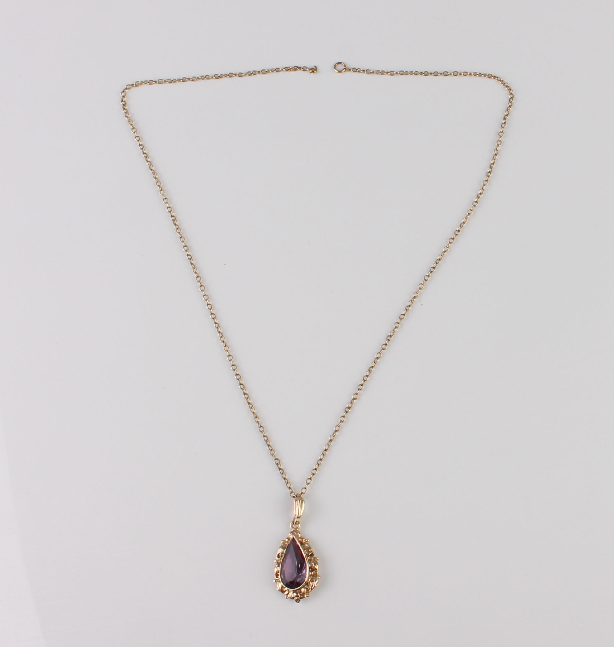 A 9ct gold and amethyst pendant - the pear cut amethyst, approx. 14.5 x 7.5mm, in a foliate scroll