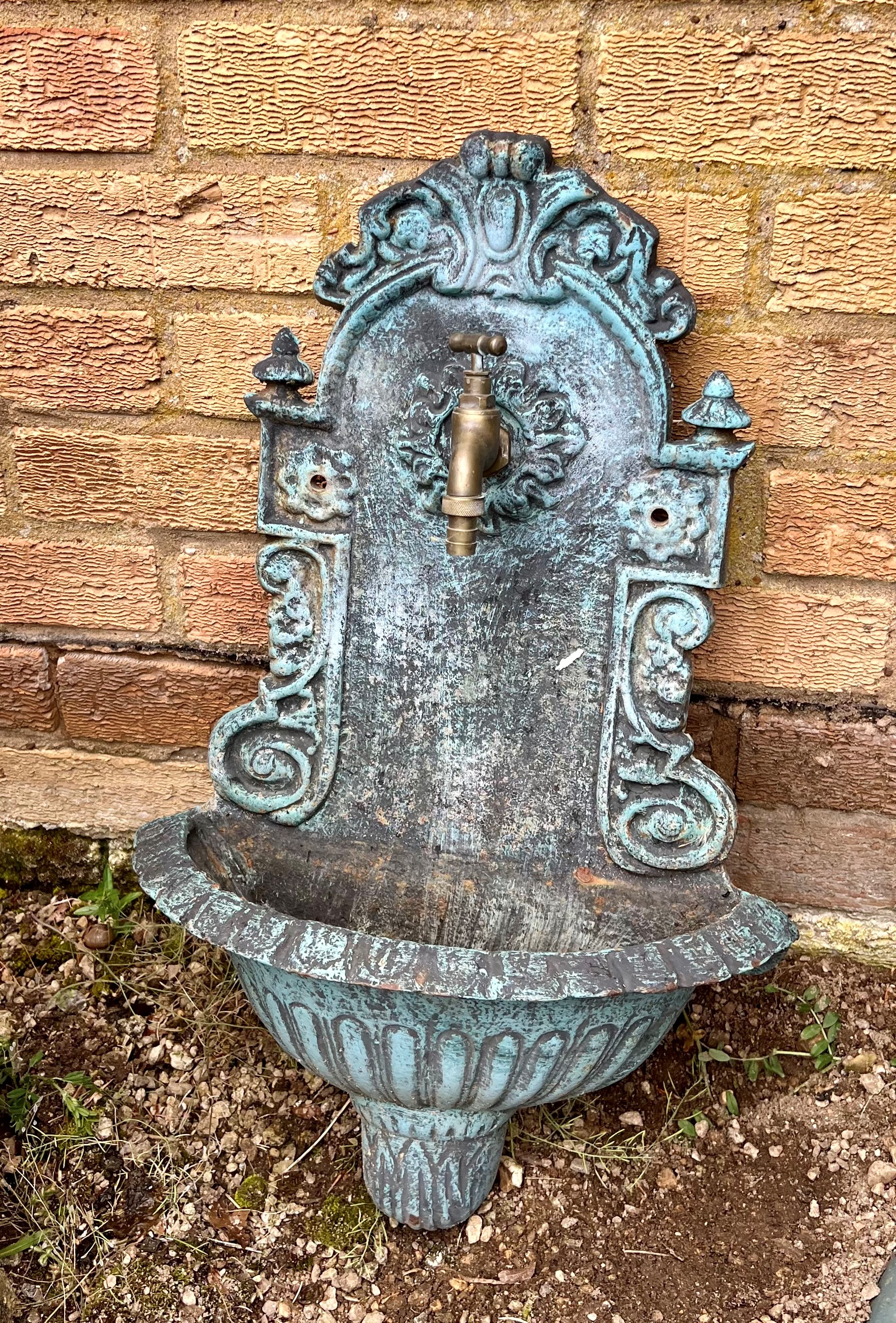 A green-painted cast-metal wall-mounted water feature - with brass tap over a semi-circular bowl,