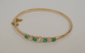 AN EMERALD & DIAMOND YELLOW METAL HINGED BANGLE WITH 4 CIRCULAR CUT EMERALDS AND 3 OLD BRILLIANT