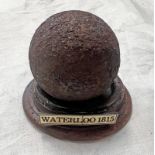 CANNON BALL ON CIRCULAR WOODEN STAND WITH PLAQUE MARKED WATERLOO 1815,