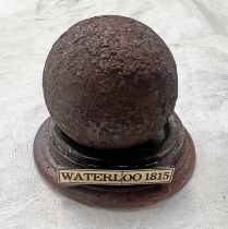 CANNON BALL ON CIRCULAR WOODEN STAND WITH PLAQUE MARKED WATERLOO 1815,