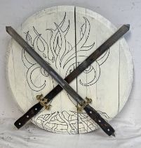 TWO DECORATIVE SWORDS WITH GILT METAL HILTS AND WOODEN GRIPS MOUNTED ON A CIRCULAR WOODEN SHIELD
