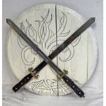 TWO DECORATIVE SWORDS WITH GILT METAL HILTS AND WOODEN GRIPS MOUNTED ON A CIRCULAR WOODEN SHIELD