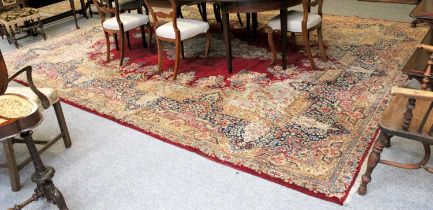 Kirman Carpet, the blood red field with a central medallion enclosed by indigo floral borders, 477cm