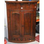 An Early 19th Century Mahogany Bow Fronted Corner Cupboard, with fielded panelled doors, shelved and