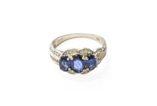 A 14 Carat White Gold Sapphire and Diamond Ring, three oval cut sapphires within a border of eight-