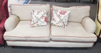 A Modern Two Seater Sofa, in beige upholstery with red piping, on turned wooden supports and with