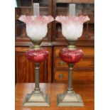 A Pair of Small Reeded Column Brass Oil Lamps, with cranberry glass reservoirs and pink frilled