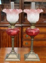 A Pair of Small Reeded Column Brass Oil Lamps, with cranberry glass reservoirs and pink frilled