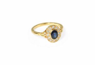 An 18 Carat Gold Sapphire and Diamond Cluster Ring, the oval cut sapphire in a yellow rubbed over