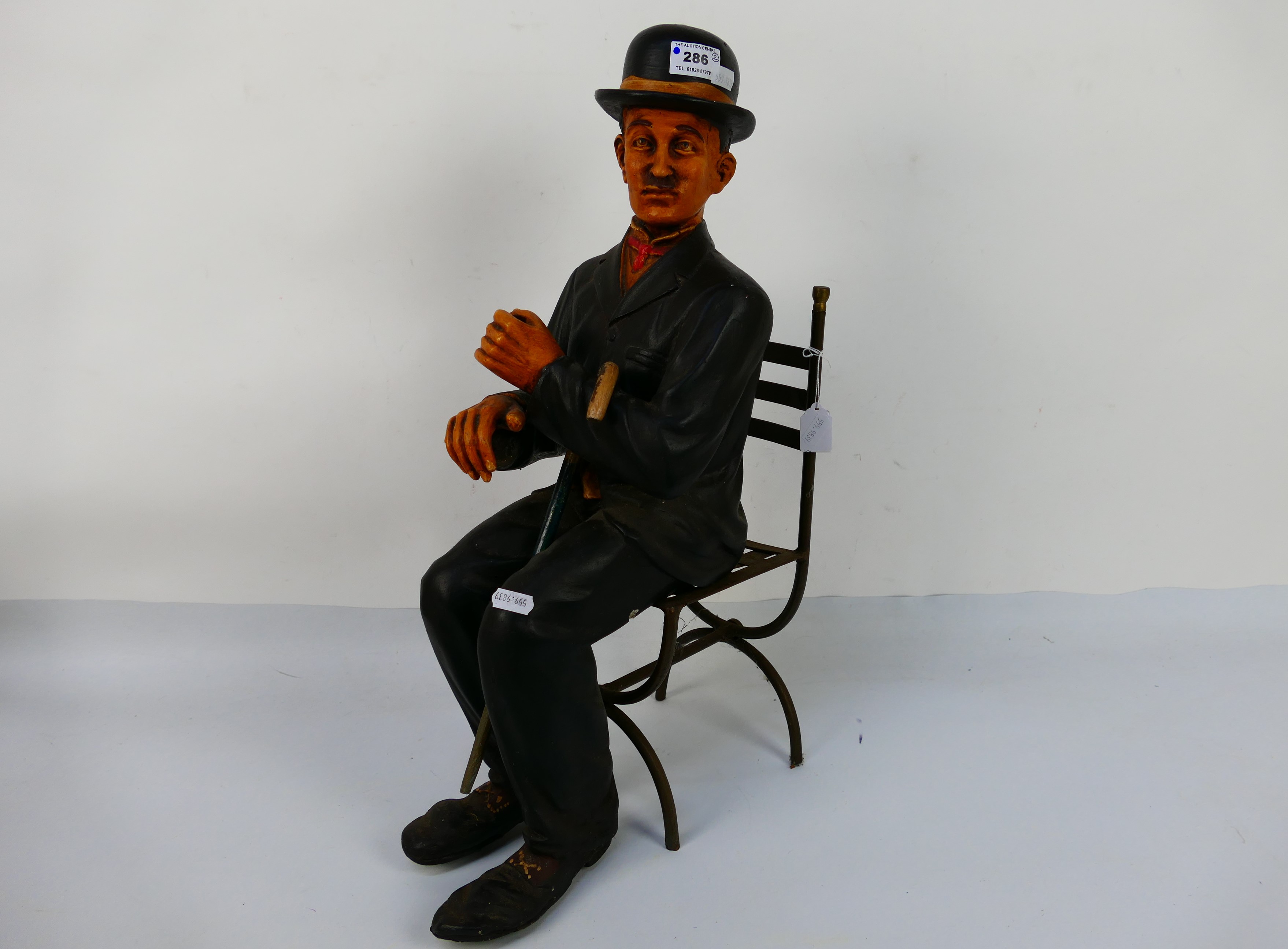 A figure depicting Charlie Chaplin in a seated pose with metal chair, approximately 57 cm (h). [2].